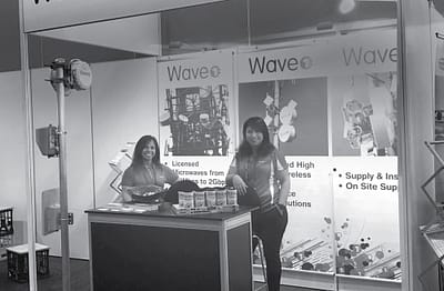 Wave 1 staff standing inside their booth in grayscale