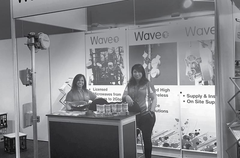 Wave 1 staff standing inside their booth in grayscale